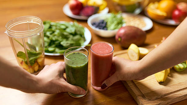 istock Hands holding two smoothies above wooden table with greens fruit and blender jar 2250139963