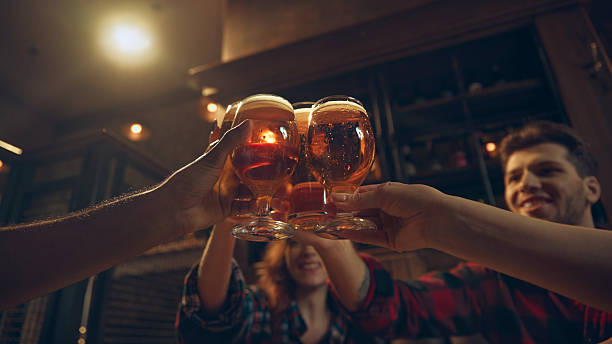istock Friends raising beer glasses with warm light in pub booth 2250142944