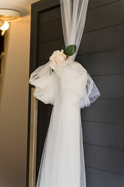 A long white fabric drapes from a door, tied in a bow. A flower rests among the folds. This setup is part of the wedding decorations in a reception area.
