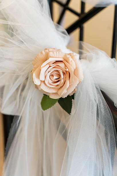 A soft rose is attached to tulle fabric on a stair railing in a bright indoor location. This setup is part of a wedding decoration. The scene shows preparations for an event.