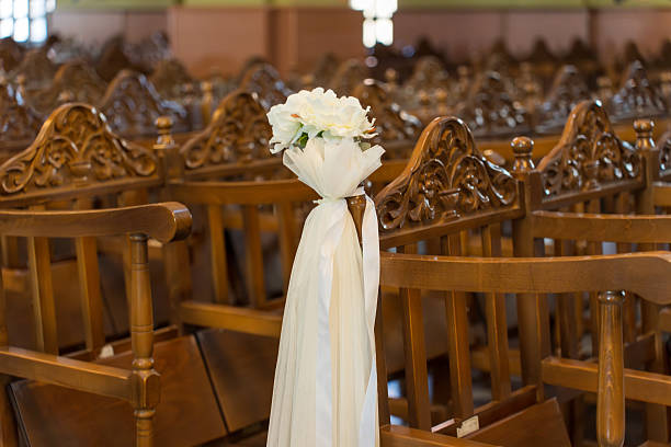 A close-up shot of two wedding chairs decorated with white fabrics in a church