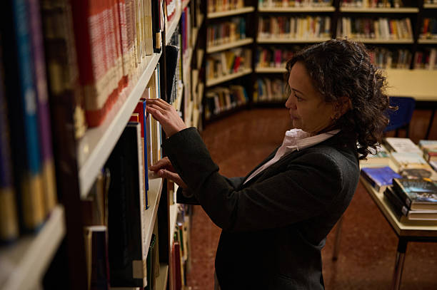 istock Woman Browsing Books in Library Aisle, Reading and Selecting a Title 2250165920