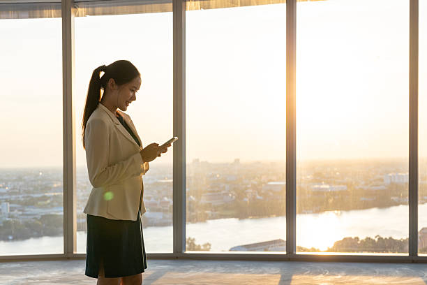 istock Businesswoman using smartphone by office window at sunset 2250166020