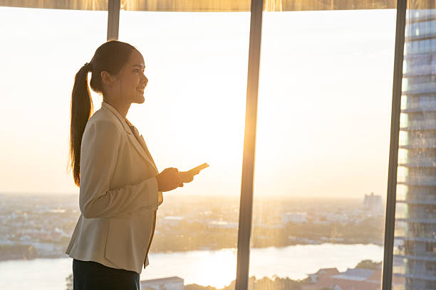 istock Businesswoman using smartphone by office window at sunset 2250166040