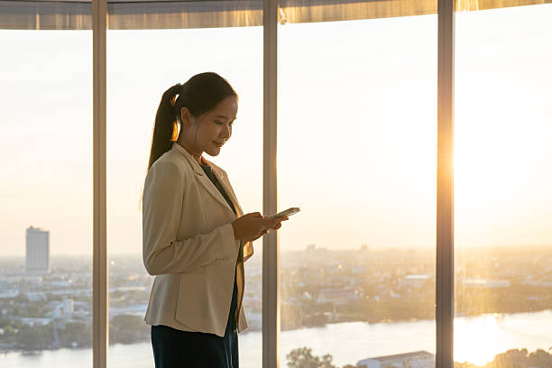 istock Businesswoman using smartphone by office window at sunset 2250166066