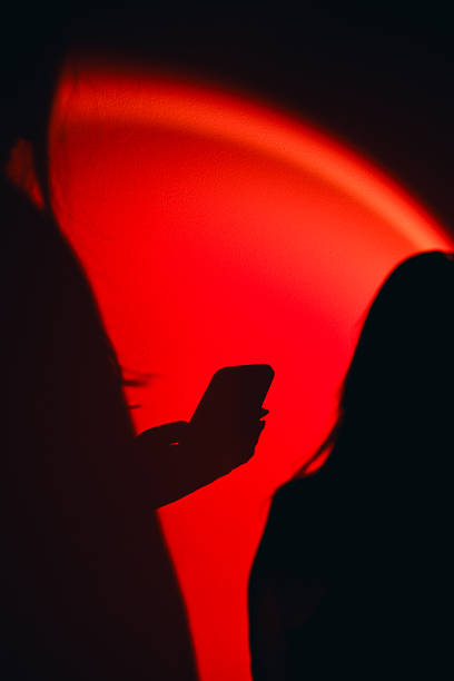 istock Woman silhouette using phone against red light wall 2250167370