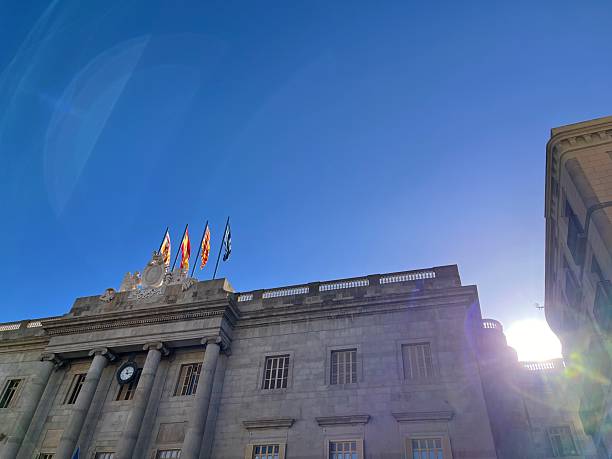Barcelona, Cataluña, Spain - October 24, 2025: Barcelona City Hall building, located in Plaça de Sant Jaume, showing its historic facade, clock, and flying flags against a clear, sunny blue sky during summer travel season