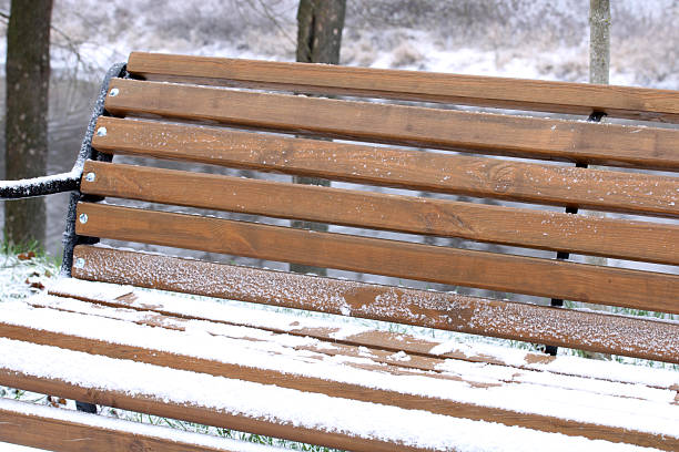 Wooden park bench covered in a light dusting of snow during cold winter weather