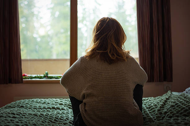 istock Woman sitting on bed looking out window contemplating 2250175791