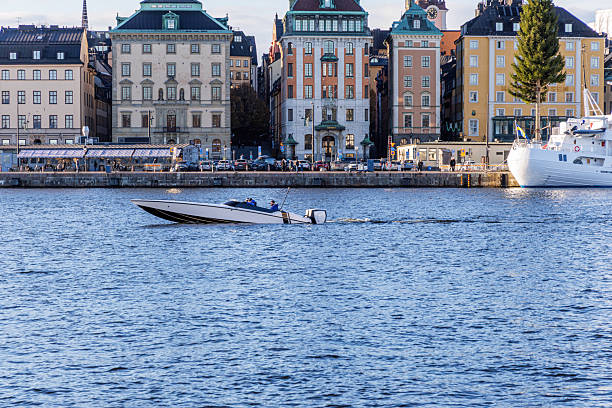 A fast, sleek speedboat creating a wake as it crosses the water in front of the historic, colorful buildings lining the quay of Stockholm's Gamla Stan.