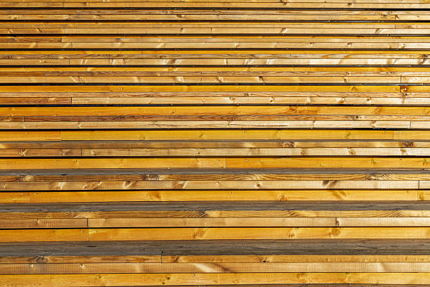 A detailed, full-frame shot of horizontally arranged light brown wooden planks, forming a textured wall, deck, or outdoor bleachers.
