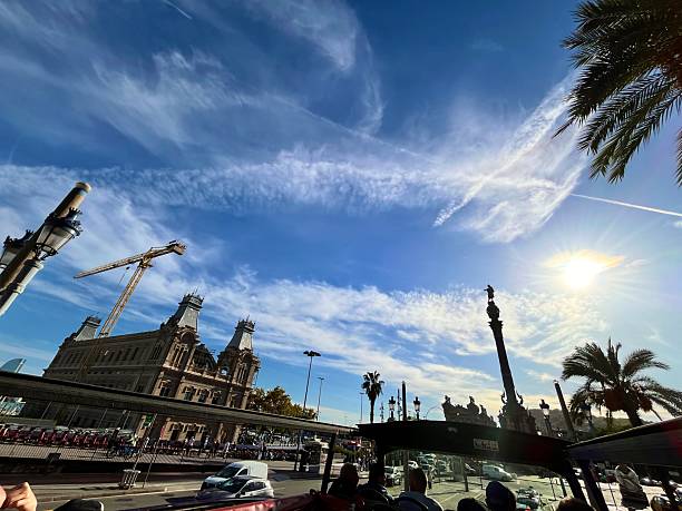 Barcelona, Cataluña, Spain - October 24, 2025: Viewing the Christopher Columbus Monument, the Port Vell customs building, and palm trees under a sunny sky while riding a tourist hop-on hop-off bus in Barcelona, Spain