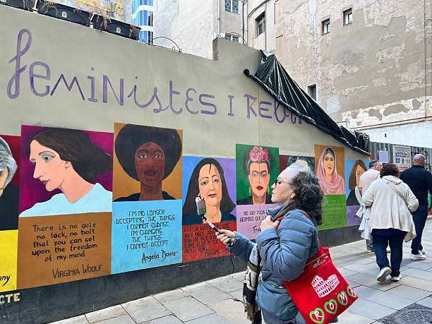 Barcelona, Cataluña, Spain - October 26, 2025: People walk a narrow Barcelona street to view a vibrant outdoor mural of feminist icons like Virginia Woolf, Angela Davis and Frida Kahlo promoting women's rights and equality