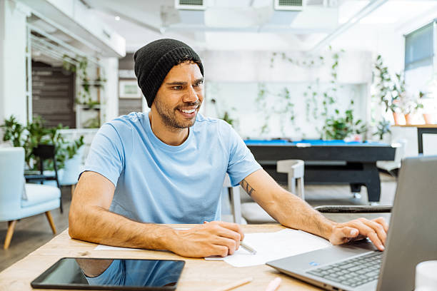 istock Smiling male entrepreneur in casual clothes working at a shared modern workspace with laptop and tablet on wooden desk 2250195361