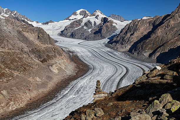 Vast sweeping Aletsch Glacier flowing between rugged alpine peaks with a small stone cairn in the foreground under a clear sky