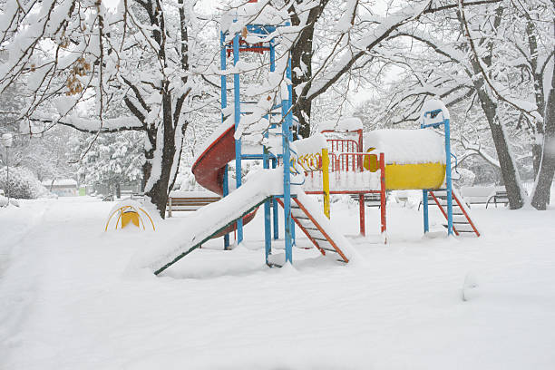 A colorful playground stands empty as fresh snow covers the equipment and surrounding park, capturing a quiet winter moment in a residential outdoor space.