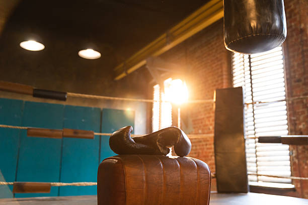 Boxing gloves lying down on boxing ring in empty gym. Equipment for fight training competition black protective boxing gloves ready for fighter winner on ring. Strength fit body workout training