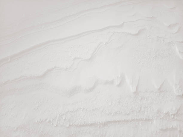 Beautiful winter background with sculptural patterns created by the wind on the snow surface. Natural snow texture in the color cloud dancer.