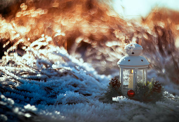 festive background with a Christmas candlestick with a candle stands on the ground covered with shiny crystals of transparent snowflakes and hoarfrost in a winter morning park