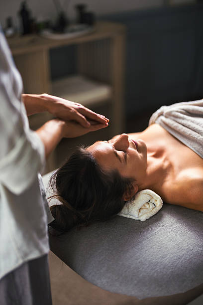 A tranquil spa treatment where a client lies on a massage table, head supported by a towel, as a therapist prepares a soothing touch above. Calm, care, relaxation, wellness, and comfort.