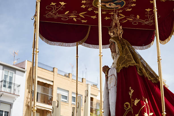 Quesada, Andalusia, Spain. April 18th, 2024. A Virgin Mary statue is carried under a red velvet canopy with gold embroidery, amid a religious procession and daylight crowds.