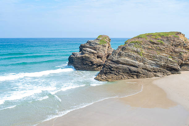 istock High-angle view of two massive sea stacks towering over pristine, sweeping sand at As Catedrais Beach, Spain. Tranquil blue water and rolling white waves complete the scenic coastal vista 2250223986