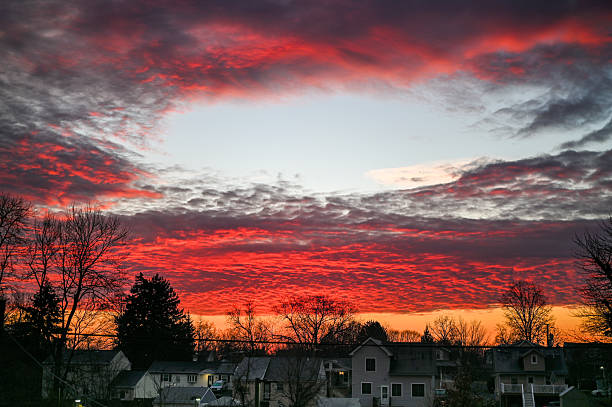 Colorful red clouds filling the sky during a dramatic sunset over a silhouetted neighborhood