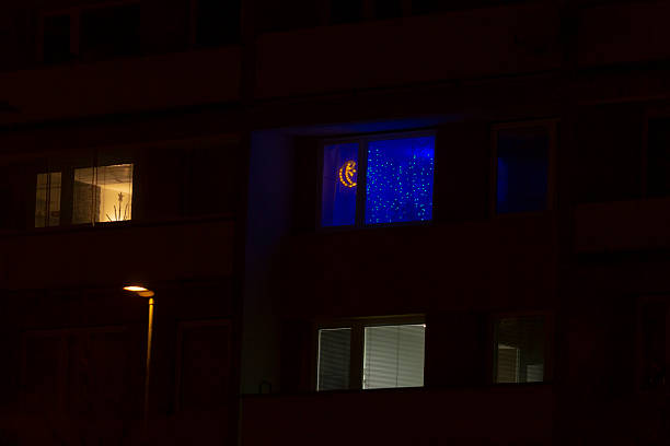 A nighttime view of a tall building with lit windows, including one with a blue backdrop and a glowing moon