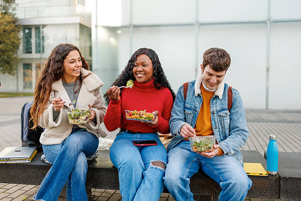 istock Students enjoying a healthy takeaway salad lunch together while sitting on a bench 2250245456