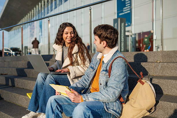 istock Diverse students working on a laptop and tablet, smiling and interacting on campus steps 2250245979