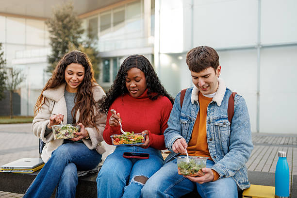 istock Diverse young people sitting outdoors, eating fresh salads and sharing a meal 2250246270