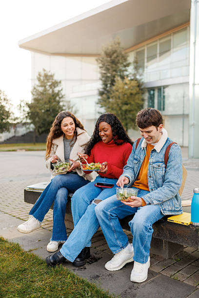 istock Diverse students happily eating takeout salads together outside a university building 2250246899