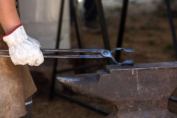 Close-up of a man wearing gloves holding blacksmith's tongs on an anvil