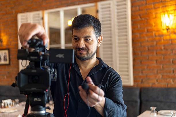istock Man videographer setting up camera on tripod, adjusting microphone for professional video production, recording content, vlogging, or live streaming event in a restaurant setting 2250261769
