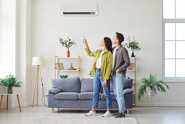 istock Happy young couple turning on air conditioning system, using remote control and changing temperature 2250263881