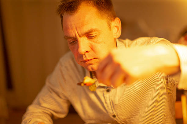 white man eating soup alone, retired teacher sits at wooden table under amber lamp stirring spoon with thoughtful expression, warm cozy kitchen evening with soft lighting, intimate contemplative