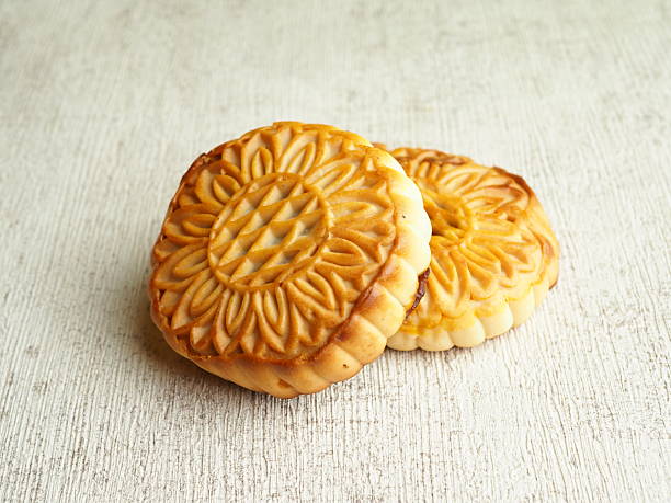 istock Two golden mooncakes sit on a textured white surface, showcasing their intricate floral designs. 2250274555