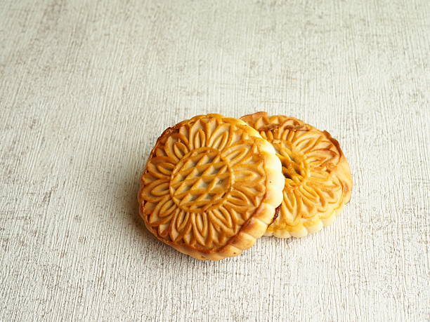 istock Two golden mooncakes with floral patterns rest on a textured, light surface in a still life shot. 2250274728