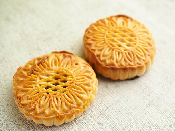 istock Two golden brown mooncakes sit elegantly on a light, textured surface in soft, natural light 2250275087
