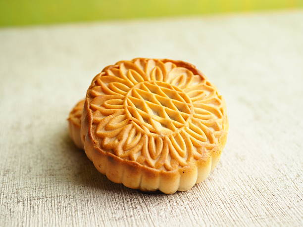 istock Golden mooncakes showcase detailed floral design, illuminated by soft light on textured surface. 2250275283