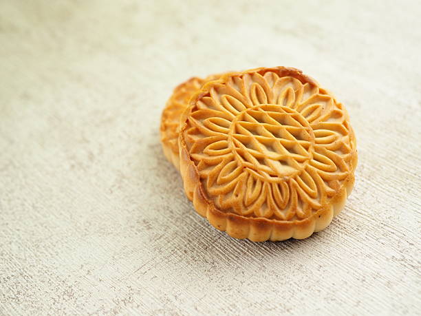 istock Two intricately patterned golden brown mooncakes are displayed on a textured cream surface. 2250275388