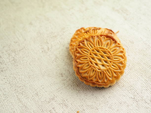 Close-up captures two golden brown mooncakes with intricate floral patterns on a textured surface.