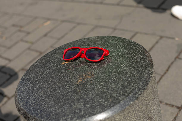 red sunglasses resting on granite bollard, abandoned on city sidewalk under warm sunlight, vibrant frame