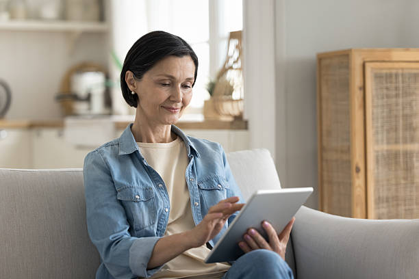 istock Attractive middle-aged woman resting on cozy sofa with tablet 2250283737