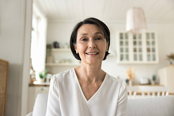 istock Attractive middle-aged woman smile looks at camera sit on sofa 2250283844
