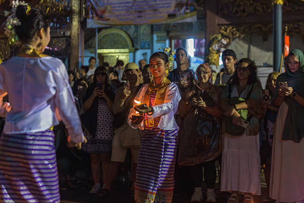 Chiang Mai, Thailand - November 05, 2025: A smiling Thai woman in traditional attire, adorned with golden jewelry and flowers, holds illuminated candles during an evening cultural celebration in