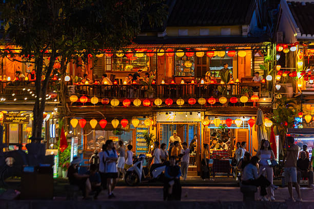 Hoi An, Vietnam - May 01, 2025: A lively evening scene in Hoi An's historic ancient town. Traditional lanterns illuminate buildings where people gather on balconies and bustling streets, enjoying the