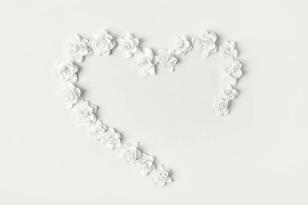 Demonstrating the colors of 2026 - Cloud Dancer. Romantic composition in shape of heart of white daffodils with satin bow on gray background. Holiday greeting card.