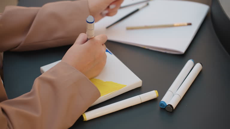 closeup hands shading yellow area on canvas with marker, layering and blending strokes for texture, focused illustrator refining tones and depth