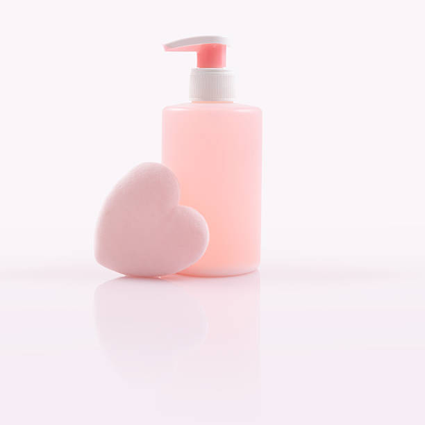 A single skincare cleanser or soap arranged with a soft pink heart-shaped makeup puff. The beauty products are isolated on a glossy reflective surface, ideal for cosmetics and skincare themes.